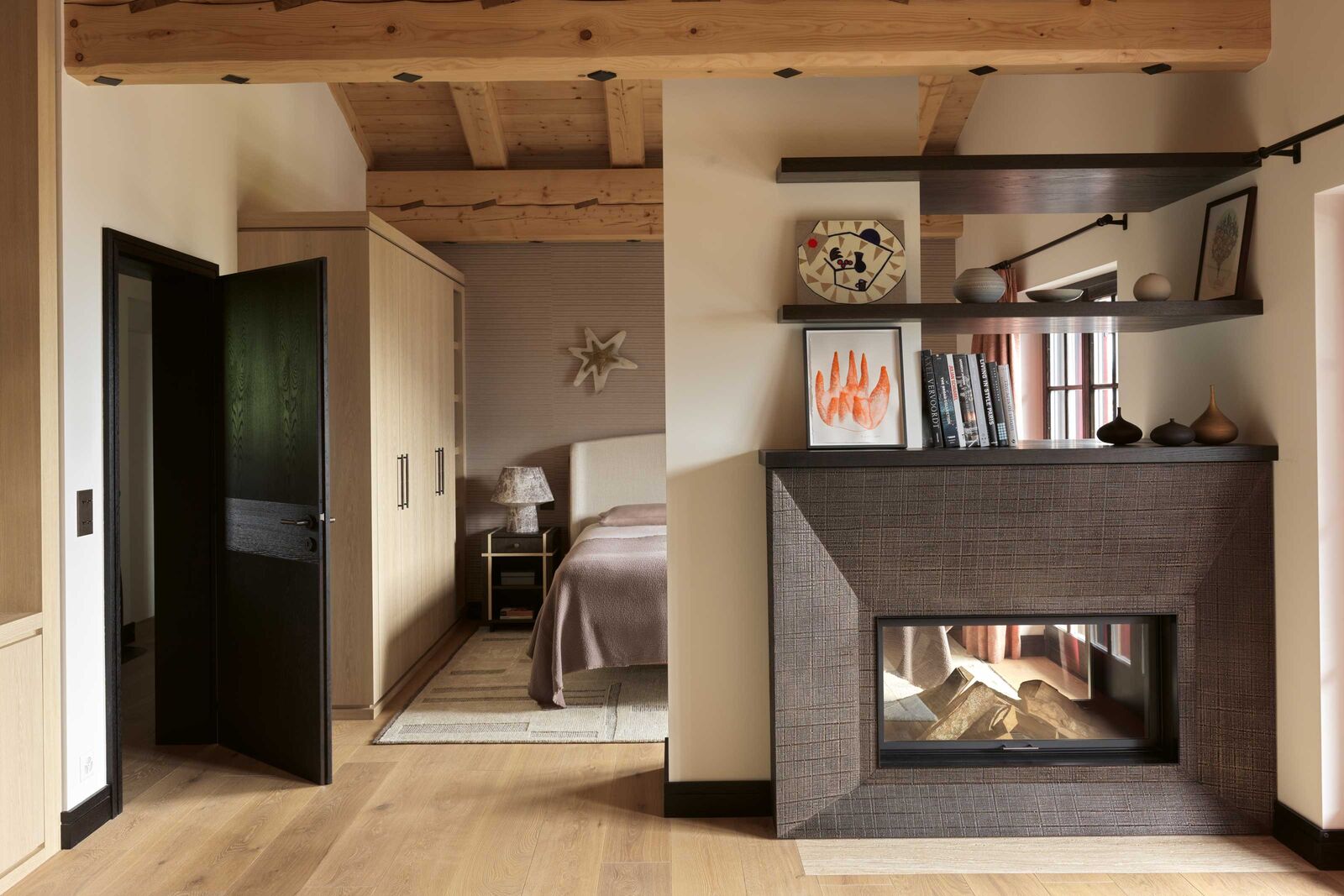 Une cheminée dessinée sur mesure par Sandra Hinton réchauffe la chambre principale. Elle est coiffée des céramiques de Sibylle Brüngger. Celles de Lilly Haas occupent l’étagère en haut à gauche. Au sol, un tapis BRICK de NEGRA Carpet & Home à Zurich apporte une touche moelleuse. Sur la table de nuit créée par Sandra, la lampe Diesel a été dénichée chez Air de Montagne à Sion. Miroir en forme d’étoile ASTER de Franck Evennou. Linge de lit Lissoy. Œuvre orange sur papier, Teresa Solar. Tableau au-dessus, Ana Prata.
