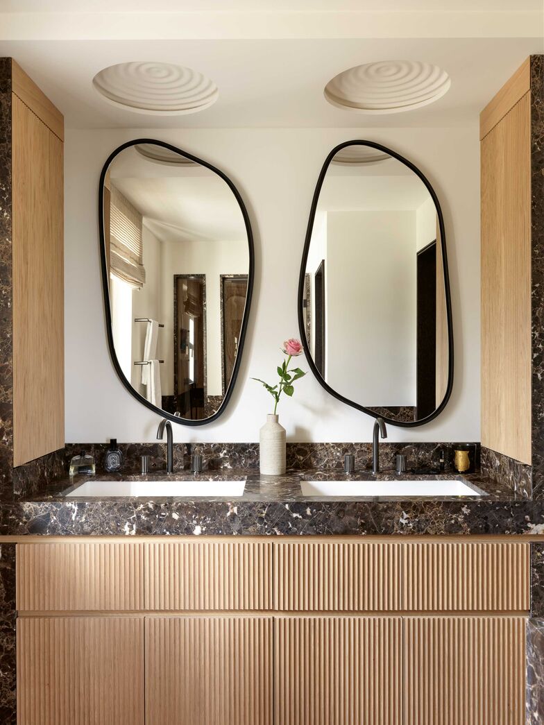 Deux miroirs signés Le Berre Vevaud animent la salle d’eau des invités. Sandra Hinton a conçu le meuble vasque en marbre emperador et en chêne. Vase Studio Roka.